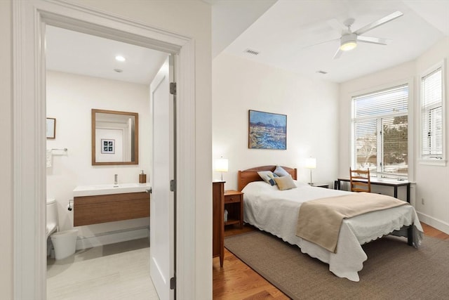 bedroom with light wood finished floors, visible vents, connected bathroom, and baseboards