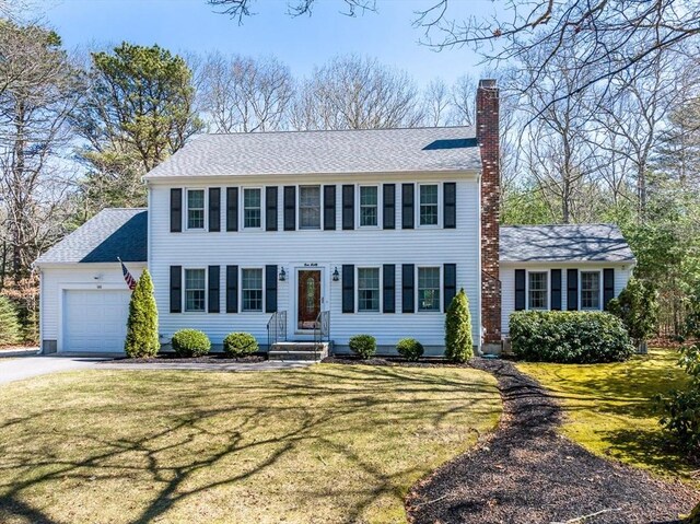 colonial-style house featuring a chimney, a garage, a front yard, and driveway