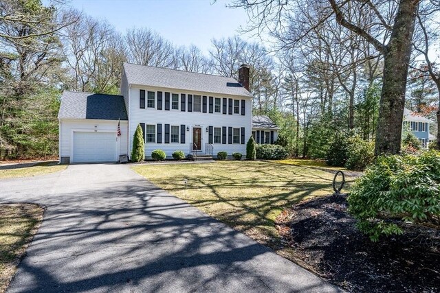 colonial home featuring a front yard, a chimney, aphalt driveway, and a garage