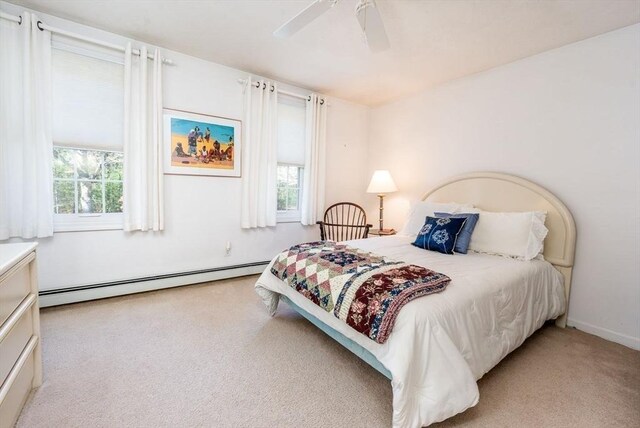 carpeted bedroom with a ceiling fan, multiple windows, and a baseboard radiator