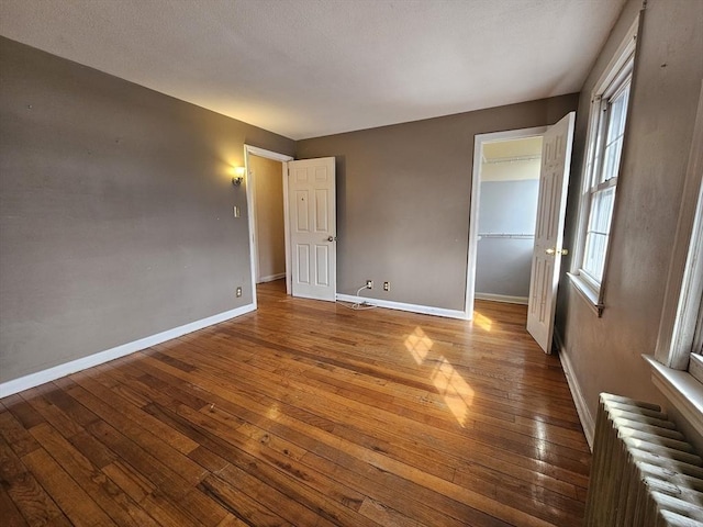 unfurnished bedroom featuring multiple windows, baseboards, radiator heating unit, and hardwood / wood-style flooring