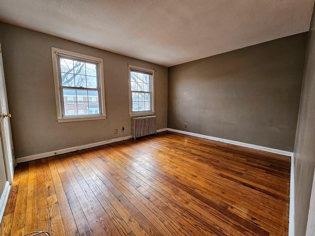 empty room with baseboards, hardwood / wood-style floors, and radiator