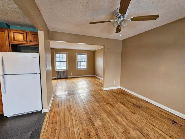 kitchen featuring brown cabinets, radiator, light wood-style flooring, freestanding refrigerator, and baseboards