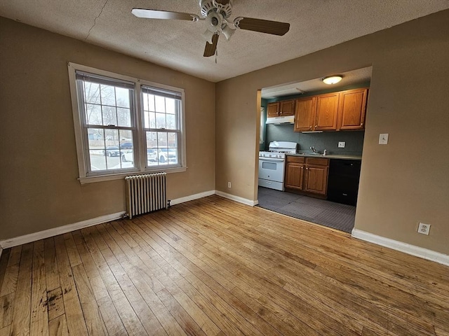 kitchen with under cabinet range hood, white range with gas cooktop, black dishwasher, brown cabinets, and radiator heating unit