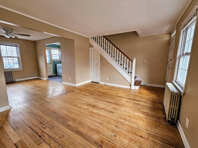 unfurnished living room with light wood-type flooring, baseboards, stairway, and radiator heating unit