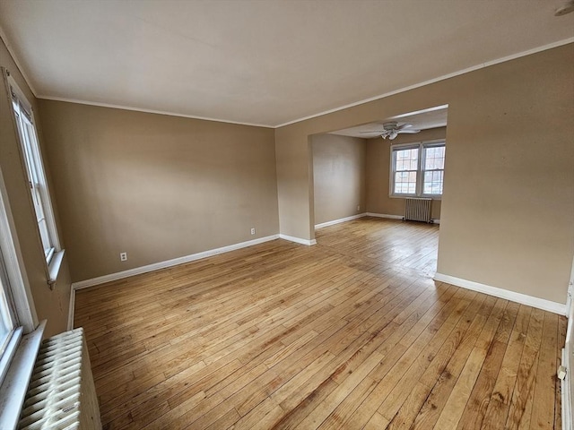 unfurnished room with light wood finished floors, radiator heating unit, ornamental molding, a ceiling fan, and baseboards