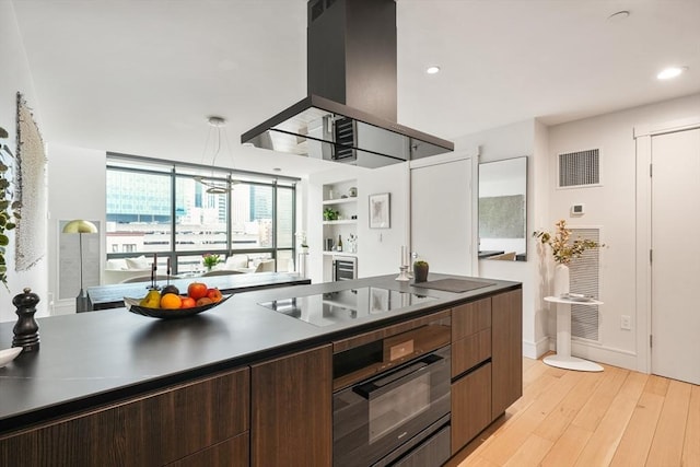 kitchen featuring island exhaust hood, visible vents, light wood-style flooring, dark brown cabinetry, and black appliances