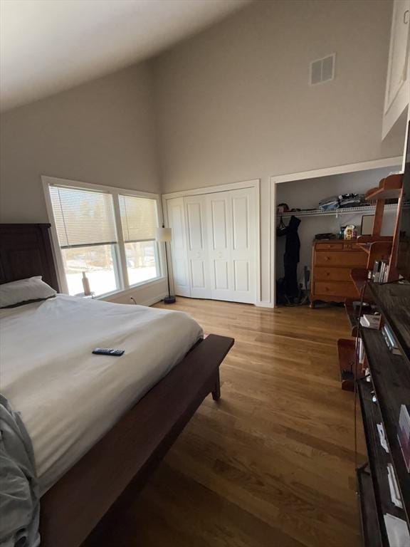 bedroom featuring high vaulted ceiling, visible vents, and wood finished floors