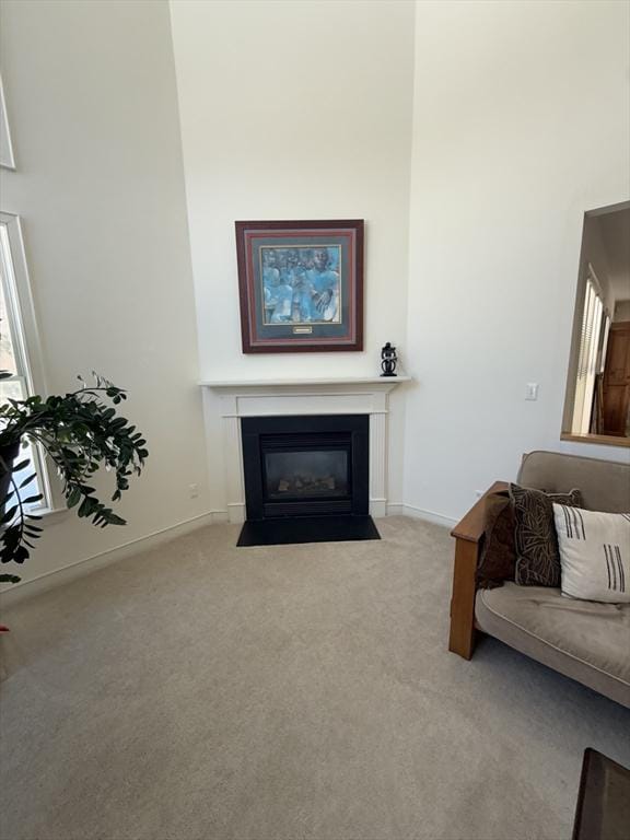 living room featuring a fireplace with flush hearth, a high ceiling, baseboards, and carpet flooring