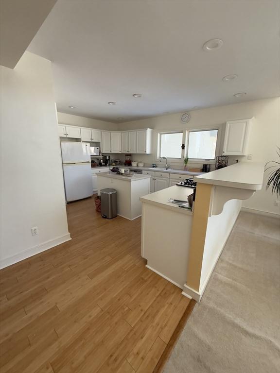 kitchen with a peninsula, white appliances, light wood-style flooring, and white cabinets