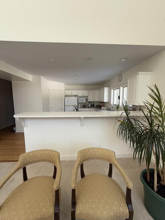 kitchen featuring a breakfast bar area, freestanding refrigerator, a peninsula, light countertops, and white cabinetry