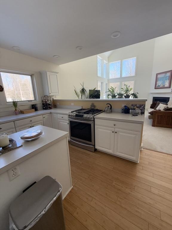 kitchen with light wood finished floors, stainless steel gas range, a fireplace, and white cabinets