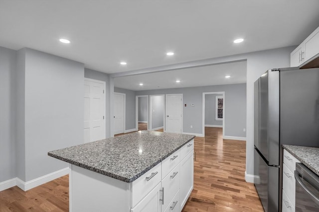 kitchen featuring a center island, light hardwood / wood-style flooring, light stone countertops, white cabinetry, and stainless steel appliances