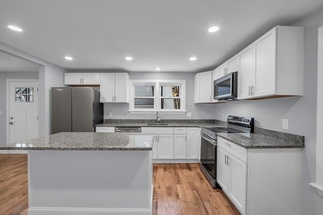 kitchen with sink, appliances with stainless steel finishes, dark stone counters, white cabinets, and light wood-type flooring