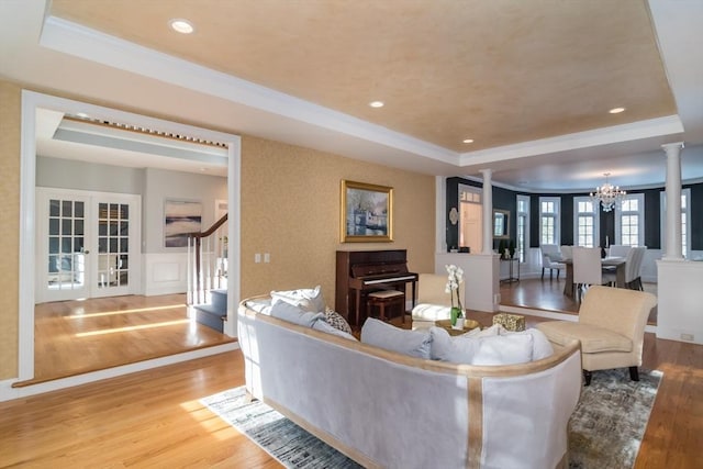 living room with french doors, a raised ceiling, decorative columns, and light wood-type flooring