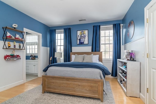 bedroom featuring multiple windows, ensuite bathroom, and light hardwood / wood-style flooring