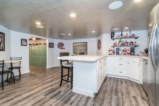 kitchen featuring hardwood / wood-style floors, white cabinetry, a breakfast bar area, kitchen peninsula, and stainless steel appliances