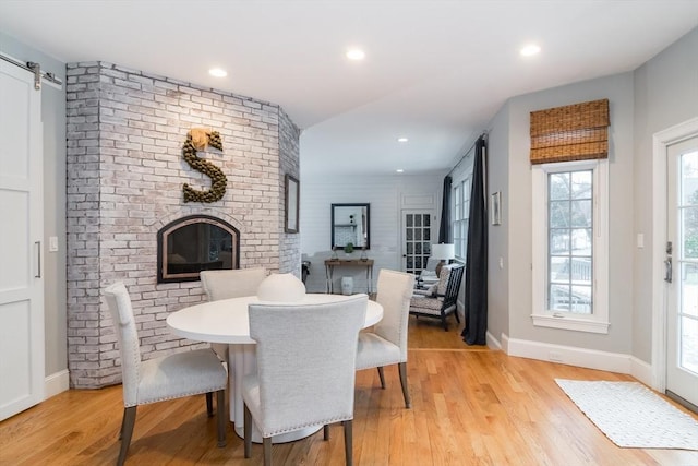 dining space featuring a brick fireplace, light hardwood / wood-style floors, and a barn door