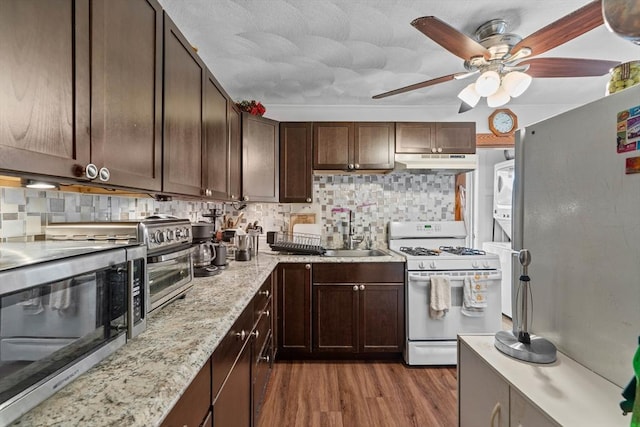 kitchen with white gas range, stainless steel microwave, under cabinet range hood, wood finished floors, and backsplash