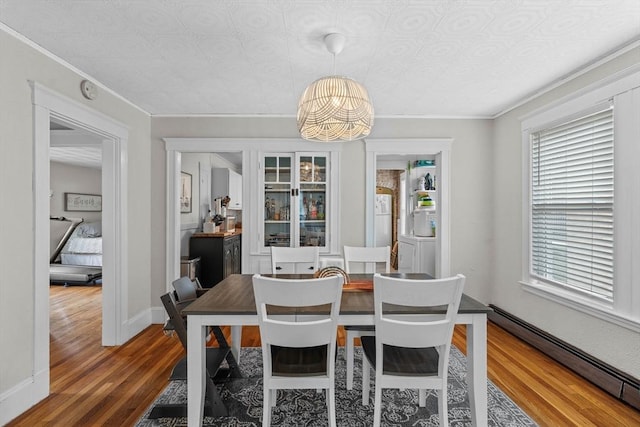 dining space with a baseboard heating unit, a chandelier, wood finished floors, plenty of natural light, and crown molding