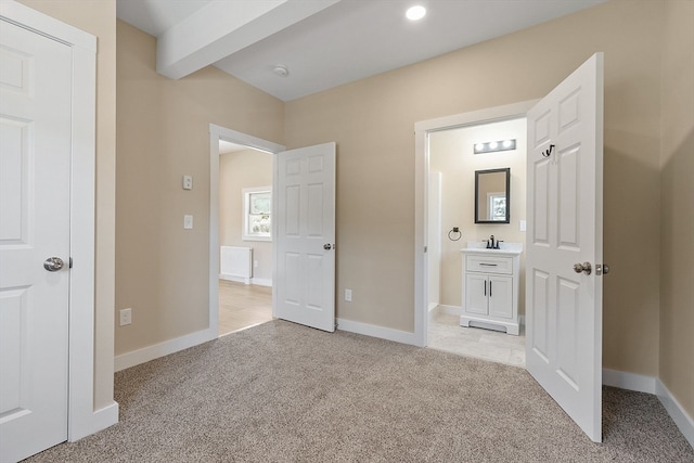 unfurnished bedroom with light colored carpet, ensuite bathroom, and beamed ceiling