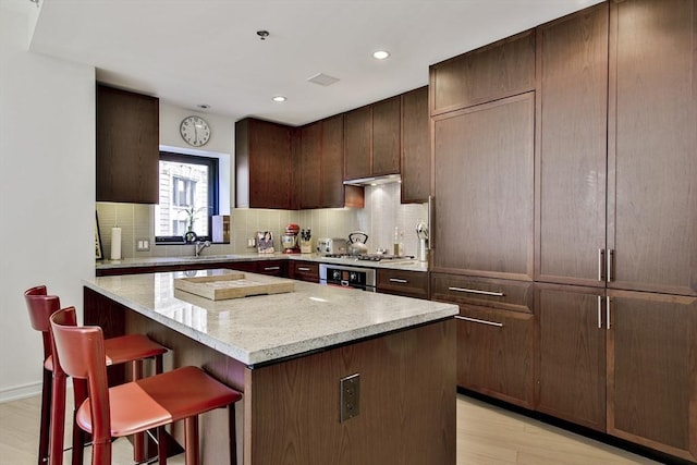 kitchen featuring dark brown cabinets, a kitchen breakfast bar, a center island, tasteful backsplash, and light stone countertops