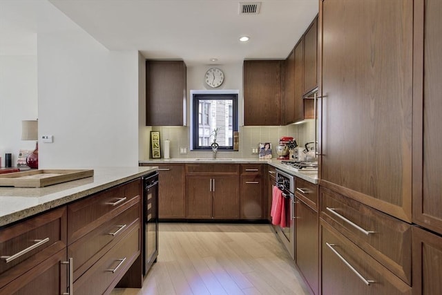 kitchen with appliances with stainless steel finishes, sink, decorative backsplash, light stone counters, and light wood-type flooring