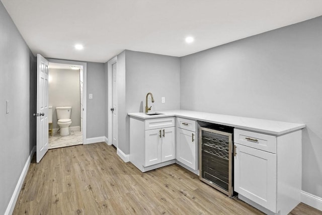 kitchen with sink, light wood-type flooring, white cabinetry, and wine cooler