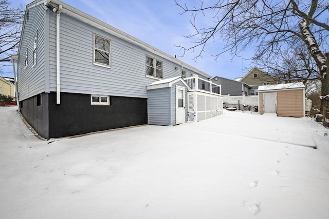 snow covered back of property featuring a storage unit