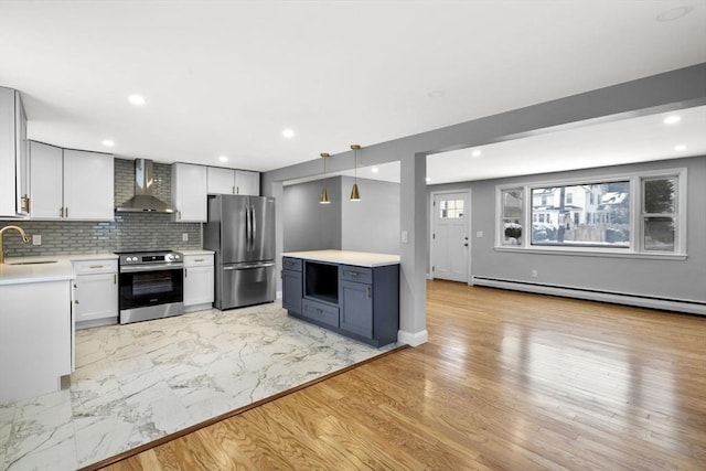 kitchen featuring appliances with stainless steel finishes, white cabinetry, wall chimney range hood, decorative light fixtures, and sink