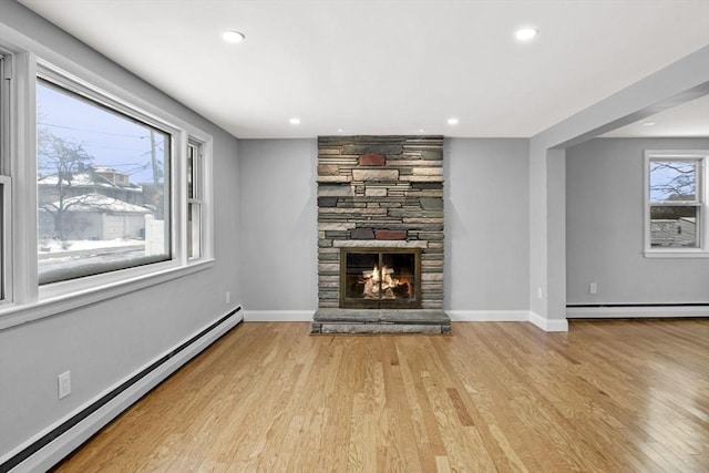 unfurnished living room featuring light hardwood / wood-style flooring, a baseboard heating unit, and a stone fireplace