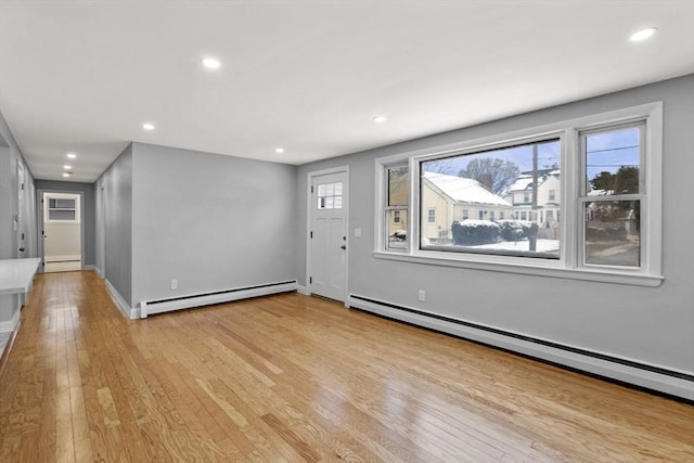 unfurnished living room featuring light hardwood / wood-style flooring, a baseboard heating unit, and a wealth of natural light