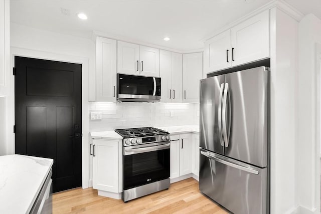 63 Oak St Unit 2, Somerville, MA 02143 - kitchen with stainless steel appliances, light wood-style floors, white cabinets, decorative backsplash, and light stone counters