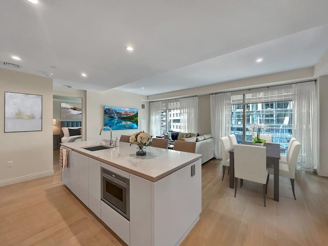 kitchen featuring sink, white cabinetry, a center island with sink, oven, and light hardwood / wood-style floors