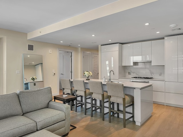 kitchen featuring tasteful backsplash, white cabinets, stainless steel gas stovetop, light wood-type flooring, and sink