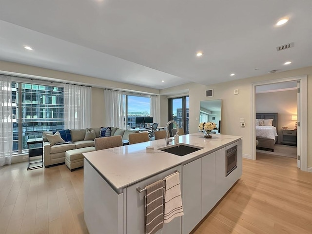 kitchen with an island with sink, sink, white cabinets, and light hardwood / wood-style flooring