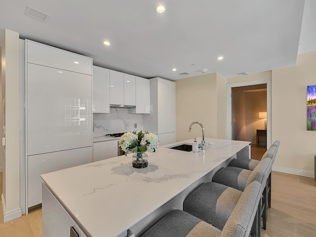 kitchen featuring light wood-type flooring, white cabinets, backsplash, and light stone countertops