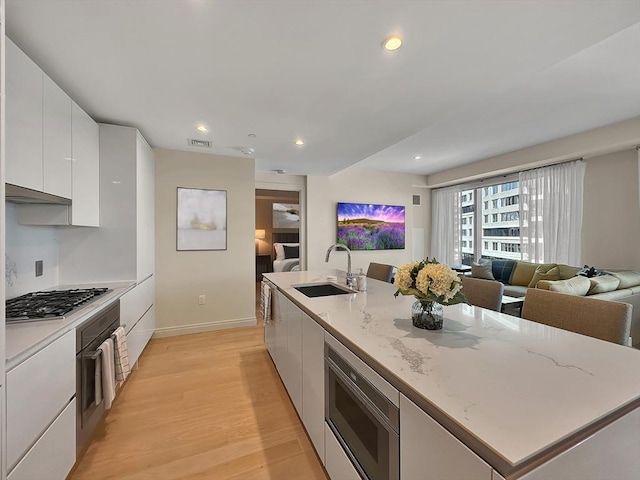 kitchen with sink, light hardwood / wood-style flooring, appliances with stainless steel finishes, a kitchen island with sink, and white cabinets