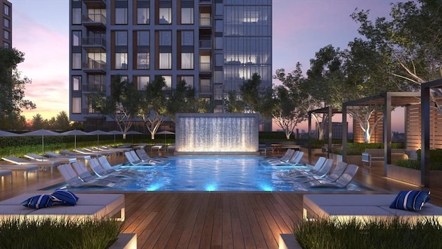 pool at dusk featuring a wooden deck and pool water feature