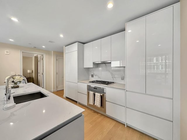 kitchen with appliances with stainless steel finishes, sink, white cabinets, decorative backsplash, and light hardwood / wood-style flooring