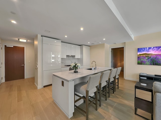 kitchen with a breakfast bar area, light hardwood / wood-style flooring, white cabinets, sink, and decorative backsplash