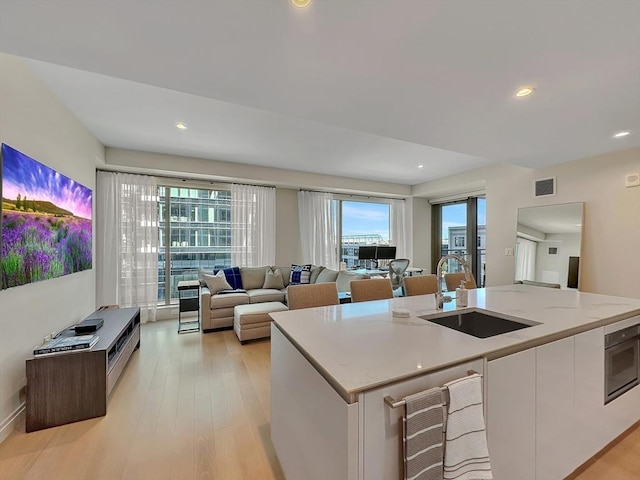 kitchen with sink, light stone counters, light wood-type flooring, an island with sink, and white cabinets