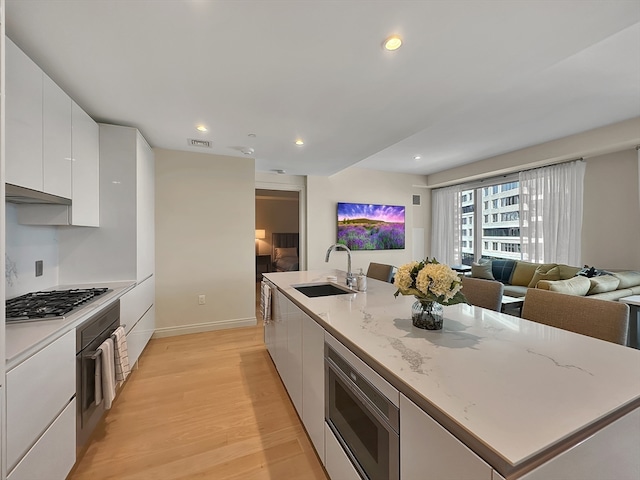 kitchen with appliances with stainless steel finishes, sink, light stone counters, light hardwood / wood-style floors, and white cabinetry