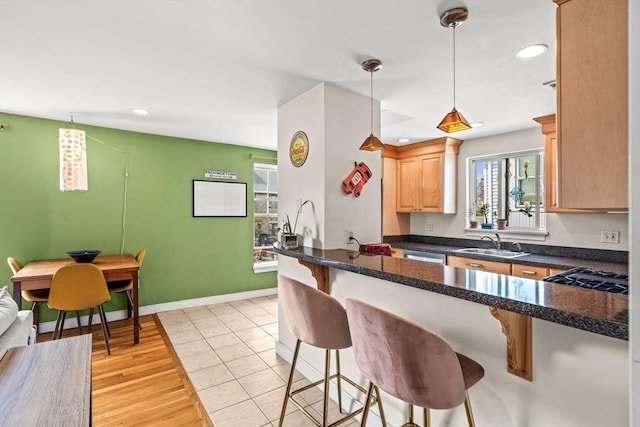 kitchen with pendant lighting, a sink, light brown cabinetry, a breakfast bar area, and cooktop