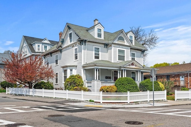 victorian-style house with covered porch, a fenced front yard, and a chimney