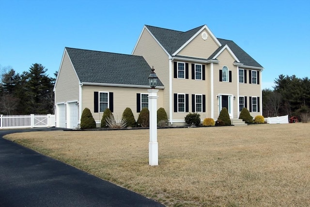 colonial house featuring a garage, fence, a front lawn, and a gate