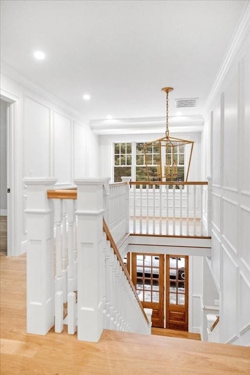 staircase with ornamental molding, wood finished floors, visible vents, and a decorative wall