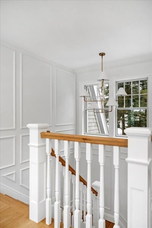 stairs with a chandelier, a decorative wall, and wood finished floors