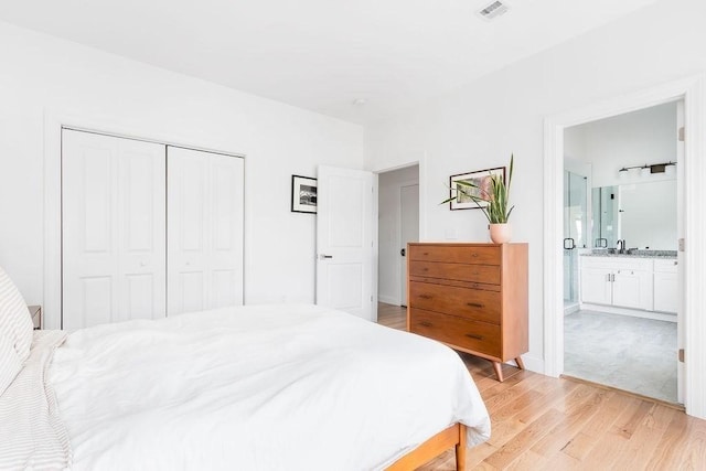 bedroom with light wood-style floors, a closet, a sink, and ensuite bathroom