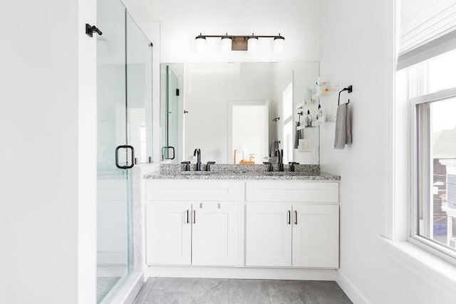 bathroom with a stall shower, double vanity, and baseboards